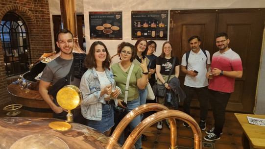 People standing in front of the copper kettles of a brewery.
