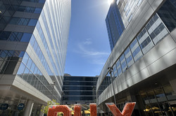 Große, orangene Buchstaben "PHX" zwischen modernen Hochhäusern rechts und links und vor blauem Himmel.  