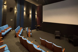 Kino Das Bild zeigt einen Kinosaal mit Sitzreihen und einer weißen Leinwand im Hintergrund.