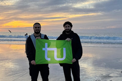 Man erkennt die beiden Storyteller am Strand bei Sonnenuntergang mit der TU Dortmund Flagge.