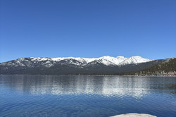 Blick auf einen See mit schneebedeckten Bergen im Hintergrund und blauem Himmel.