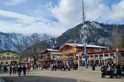 Hier sieht man viele Hütten aus Holz. Dahinter erkennt man schneebedeckte Berge.