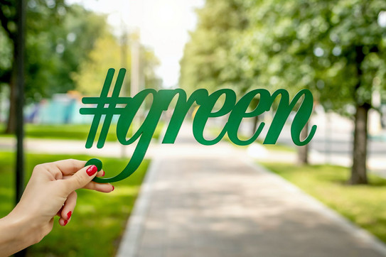 eine Person hält den Schriftzug "#green", mit einem Park im Hintergrund an einem sonnigen Tag