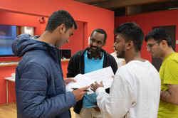 A group of international students are standing together and talking. They show each other something on pieces of paper.
