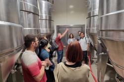 People are standing in the storage room of a brewery in front of huge metal barrels.