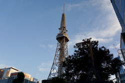 Metallener Turm umgegben von Restaurants, hohen Häusern mit Glasfassaden und Bäumen. 