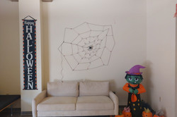 Halloween Deko im Wohnheim Hier sieht man ein Zimmer mit Sofa und darüber ist ein Spinnennetz als Deko, genauso wie eine aufblasbare Hexe und mehrere Kürbisse.
