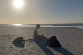 Auf dem Bild sieht man Jonas B. wie er am Strand sitzt