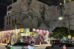 Wynwood Miami Es zeigt ein Gebäude, worauf Menschen mit geschlossenen Augen und gehobenen Händen abgebildet sind, davor ein Strommast und eine bunt bemalte Mauer