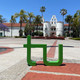 San Diego State ein TU Logo steht auf dem Campus der SDSU vor einem weißen Gebäude im mexikanischen Stil. Palmen sind auf beiden Seiten vom Gebäude