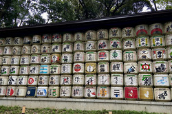 Eine Wand aus Fässern, die übereinander gestapelt und nebeneinander aufgereiht sind. Die Fässer tragen Schriftzeichen und Muster. 