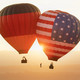2 hot air balloons, one with the German flag and one with the US flag, float in the air