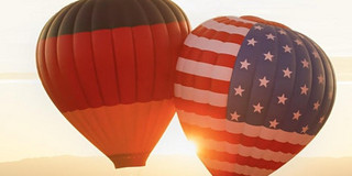 2 Heißluftballons, eins mit der deutschen Flagge und ein mit der US-Flagge, schweben in der Luft