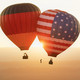 2 hot air balloons, one with the German flag and one with the US flag, float in the air