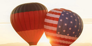 E_112021_Hasso-Plattner_cdn.evbuc.com_images_166610739.jpg 2 Heißluftballons, eins mit der deutschen Flagge und ein mit der US-Flagge, schweben in der Luft
