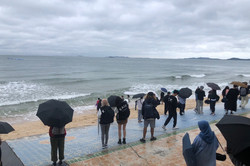 Hier sieht man Menschen mit Regenschirmen am Strand. 
