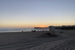 Strand im Vordergrund mit untergehender Sonne über dem Meer im Hintergrund 