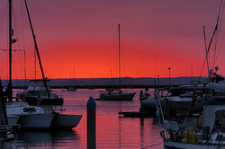 Hier sieht man einen Hafen während eines Sonnenuntergangs. Der Himmel ist rot/orange. 