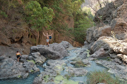 Hier sieht man den Studenten und eine andere Studentin, die zusammen über Felsen in einem Fluss klettern.