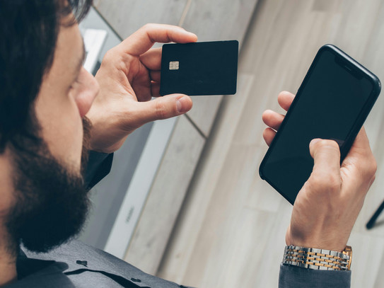 Ein Mann der eine Bankkarte und ein Handy in den Händen hält
