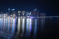 Aussicht auf die Küste von Busan bei Nacht. Die Lichter der Stadt spiegeln sich im Wasser. 