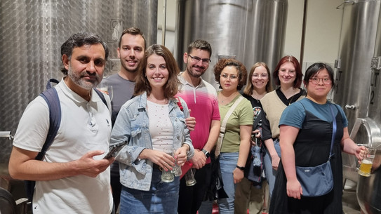 A group of people standing in front of the huge metal barrels of a brewery. 
