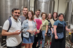 Eine Gruppe von Menschen steht vor den großen Metallfässern einer Brauerei.