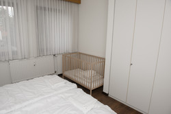 Ein Blick in das Schlafzimmer eines Apartments im Gästehaus. Man erkennt ein Kinderbett, einen Schrank und Teile eines Betts.