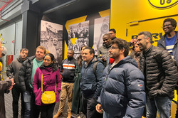 Menschen stehen in den Gängen eines Fußballstadions und hören jemandem zu.