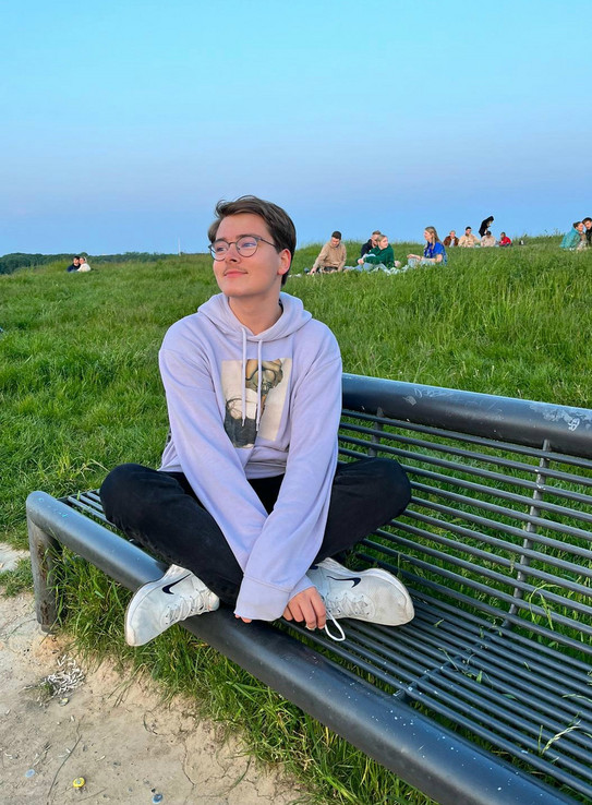 Profilfoto Lars Hier sieht man den Studenten im Schneidersitz auf einer Bank in einem Park sitzen.