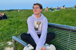 Profilfoto Lars Hier sieht man den Studenten im Schneidersitz auf einer Bank in einem Park sitzen.