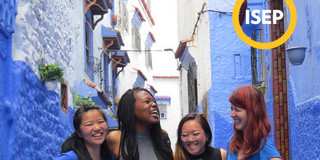 Four persons standing in between blue buildings smiling