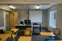 Hier sieht man einen Klassenraum bestehend aus Holztischen und -stühlen.