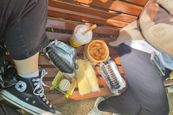 Lunchen mit einer Freundin Man sieht zwei Personen auf einer Bank sitzen und auf der Bank sind verschiedene Speisen aufgestellt.