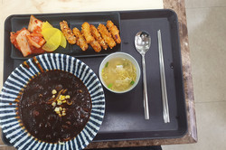 Man sieht ein koreanisches Gericht namens Jajjangmyeon.  Dazu Kimchi, gebratene Fleischstreifen, Rettich und eine kleine Suppe. 