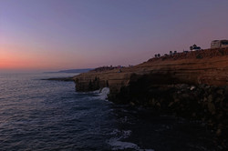 Sunset Cliff Man erkennt einen schönen Sonnenuntergang. Der Himmel ist rosa gefärbt und man sieht sowohl Klippen, als auch Wasser.
