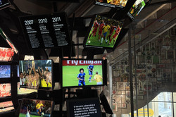 Blick in einen Museumsraum mit vielen Bildschirmen bis unter die Decke. Fußball-Spiele laufen.