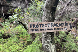 Clean Blue Mountains Ein Baum mit einem Schild mit dem Text "Protect Paradise. Please take your rubbish"