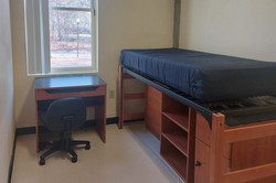 Leeres Wohnheimzimmer Hier sieht man ein Bett und einen Schreibtisch mit Stuhl in einem kleinen Zimmer.