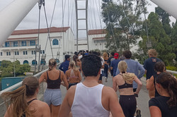 Running Club Man erkennt viele Läufer*innen, die über eine Brücke joggen.