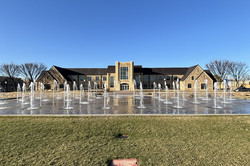 Eine Wiese vor einem Gebäude auf dem Campus - darin ist ein großer flacher Brunnen eingebaut. Wasser spritzt an vielen Stellen hoch.