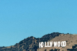 Auf dem Bild ist das Hollywood Sign aus der Ferne fotografiert. Im Hintergrund erkennt man einen blauen Himmel.