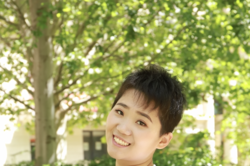 Porträt einer jungen Frau mit kurzen Haaren vor Bäumen