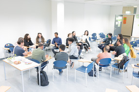 A larger group of international students sits in two circles of chairs and the students talk. 