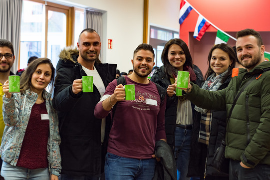 a group of international students with TU Dortmund University cups in their hands, smiling into the camera