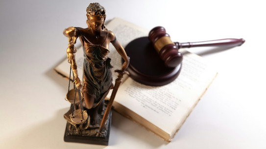 Eine Statue der Justitia und ein offenes Buch, auf dem ein Hammer aus Holz liegt.