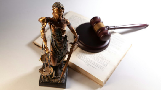 A statue of Justitia and an open book, on which a gavel has been placed.