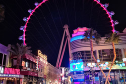 Hier sieht man ein bunt beleuchtetes Riesenrad und beleuchtete Shops. 