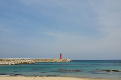 Hier sieht man einen Strand mit einem Steg, an dessen Ende ein roter Turm steht. 
