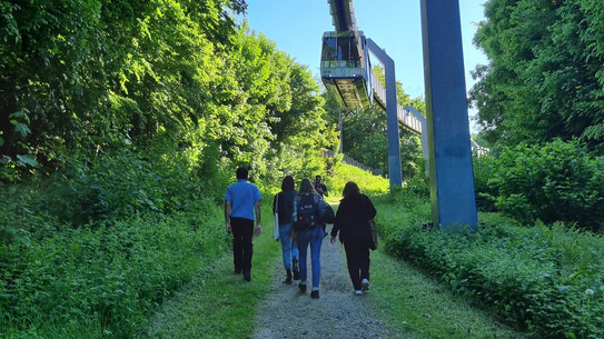 Menschen laufen unter der H-Bahn her. 